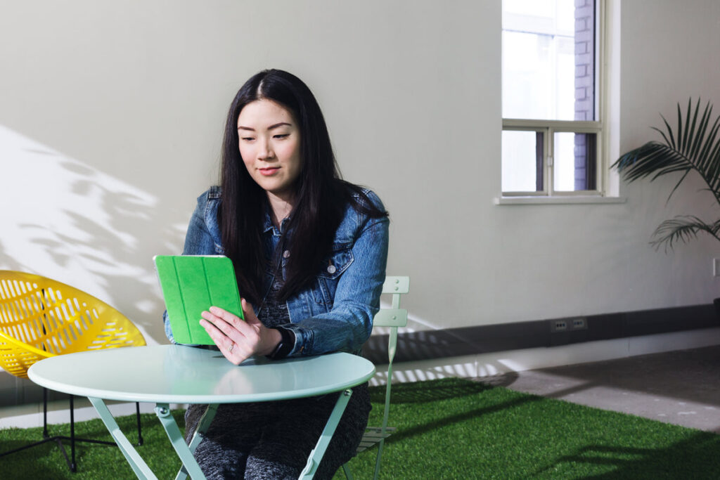 Femme assise à une petite table ronde pliante blanche en train de comparer des modèles de tables pliantes sur une tablette numérique