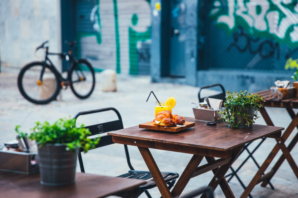 Table de jardin pliante style bistro avec chaises metalliques sur une terrasse extérieure, avec des plantes vertes